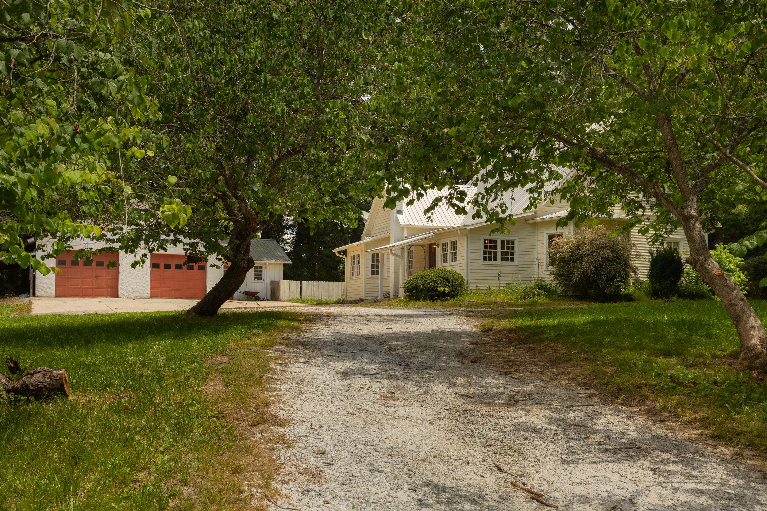 910 historic farmhouse for sale at 100 Cannon Drive in Hendersonville NC featuring a gravel driveway, mature trees, and detached 2-car garage